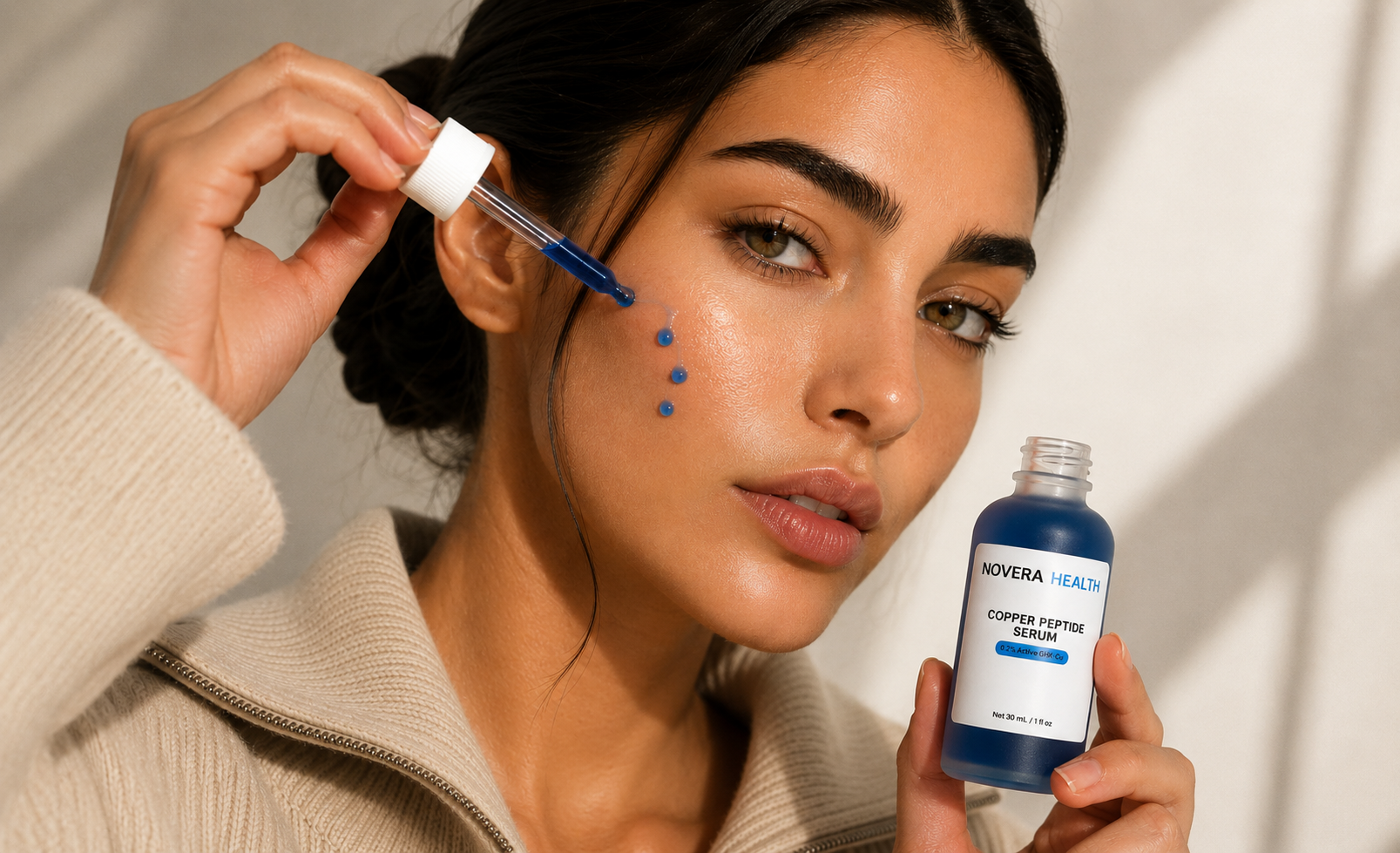 A woman applies a blue serum dropper to her cheek while holding a bottle of NOVERA HEALTH Copper Peptide Serum. The image features a clean, minimalist background with soft shadows, highlighting the product and its use.