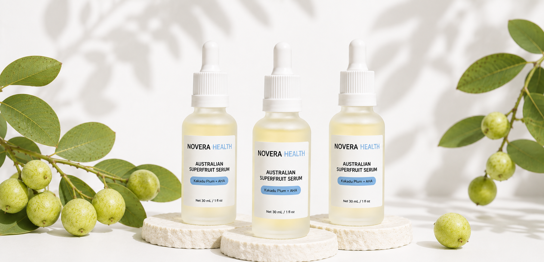 Three dropper bottles of NOVERA HEALTH Australian Superfruit Serum arranged on white textured stands, surrounded by green amla fruit branches and leaves against a bright white background with soft leaf shadows.